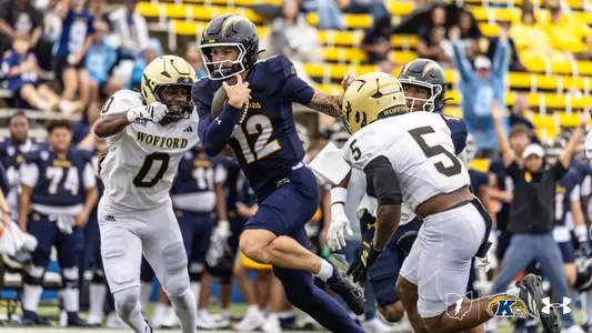 Action photo of a Kent State football player wearing number 12 running with the football past Wofford defenders during a game.