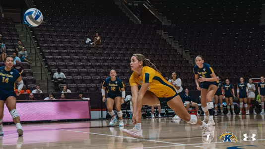 Kent State volleyball player Lesley Furuta digs a low ball during a match, with teammates numbers nearby on the court at Virginia Tech's arena.