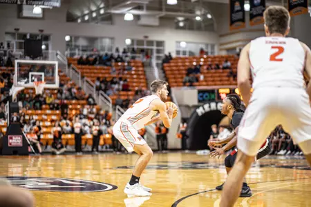 Mercer men's basketball player wearing a white jersey holding the ball in front of him while a defender stands facing him