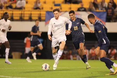 Mercer men's soccer player in a white jersey with a UNCG player in a navy jersey standing behind him