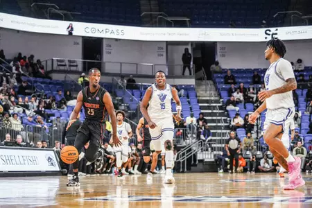 Mercer men's basketball player wearing a black jersey dribbling toward the endline while two defenders stand nearby