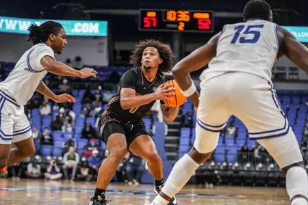 Mercer men's basketball player wearing a black jersey holding the basketball in both hands looking forward while a GSU player in a white jersey looks to block him
