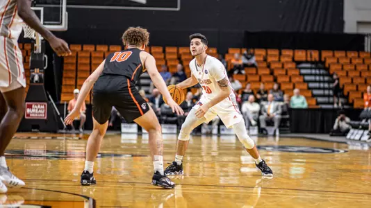Mercer men's basketball player wearing a white jersey dribbling basketball with a defender standing in front of him