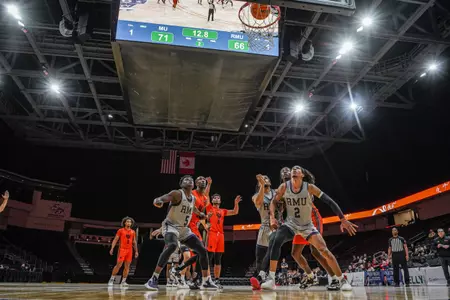 Basketball players in orange and gray jerseys look up at the basket as the basketball goes into the net