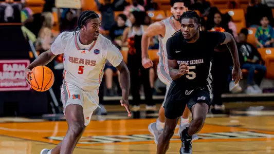 Jalyn McCreary dribbling a basketball while a Middle Georgia State defender runs alongside him