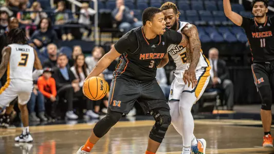 Shannon Grant holding the basketball in his right hand trying to fend off a defender on his left side at the top of the paint