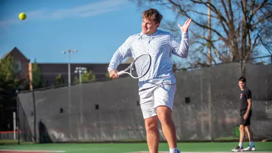 Andrew Branicki jumping to hit the tennis ball with the racket in front of his chest in his right hand