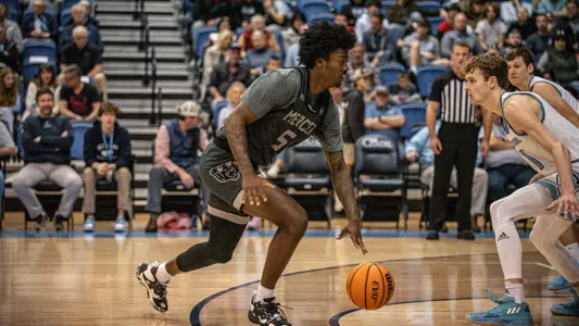 Jalyn McCreary in the middle of dribbling the basketball with his left hand while a defender watches on the side