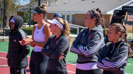 Women's tennis players watching a teammate finish playing