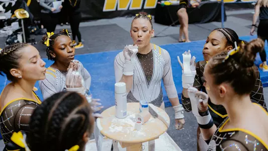 The 2025 Mizzou gymnastics team surrounding the chalk bay during the Black & Gold Intrasquad meet.