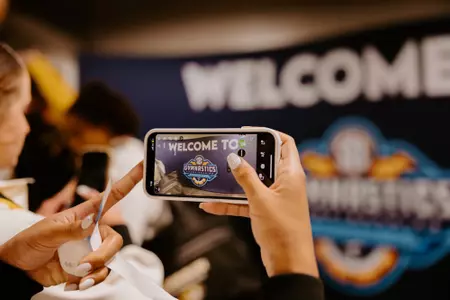 A Mizzou gymnast taking a photo of the SEC Championship sign during the team's practice session on March 21, 2025, at Legacy Arena. Photo by: {Kylie Daniel}