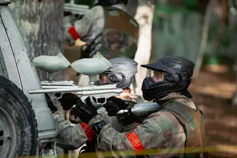 Two paintball players, both crouched and aiming their gun