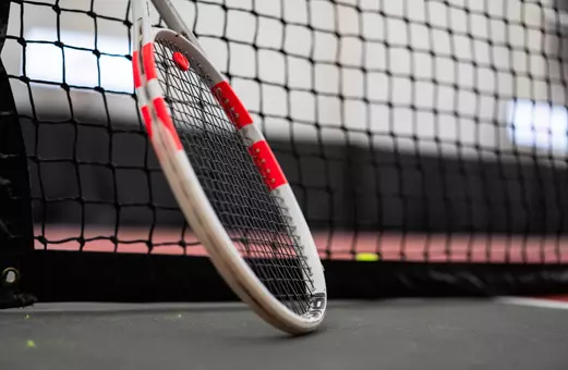 Tennis racquet leaning against the net on the indoor courts.