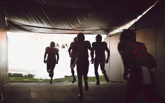 Football players from Oklahoma State run out of the tunnel before a game.
