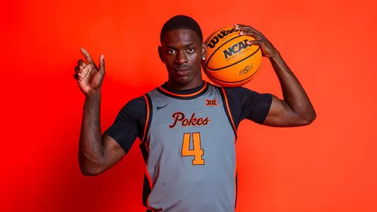 Kashie Natt poses for a photo in a grey Oklahoma State jersey against an orange background