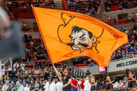 A cheerleader waves a large, orange flag showing Pistol Pete at an Oklahoma State basketball game in Gallagher-Iba Arena.