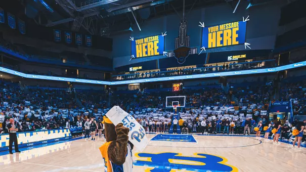 A photo of the videoboards above the IC Light Baseline club in the Petersen events center with "your message here" displayed on the boards.