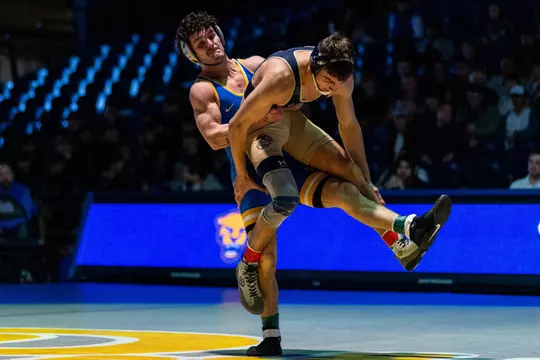A Pitt wrestler holding a navy wrestler in the air