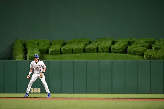 A pitt baseball player stands in the foreground with the Pirates hedge in the background behind him at PNC park