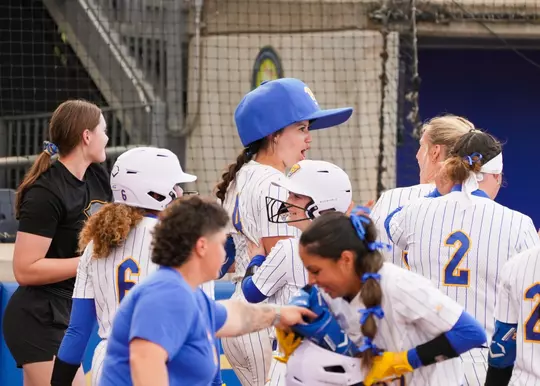 A pitt softball player is escorted off the field by her teammates after hitting a walk off grand slam, she wears an un-ordinarialy large version of a baseball cap