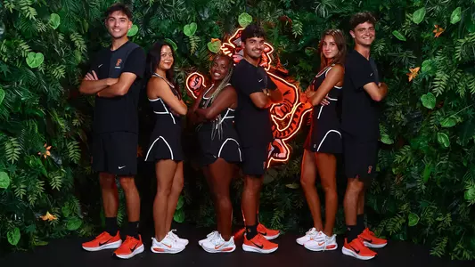 M/W tennis players stand back-to-back against the jungle screen. LtoR: Evan Wen, Bella Chhiv, Tsehay Driscoll, Landon Ardila, Alice Ferlito, Aleksandar Mitric