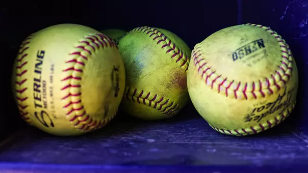 Three yellow softballs sit in the dugout of QU Softball Field