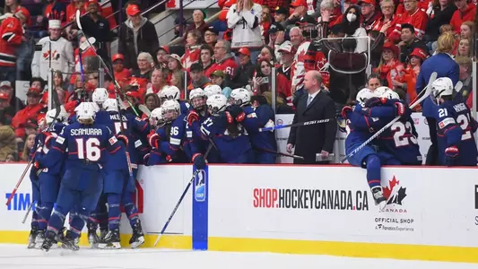 Assistant coach Brent Hill stands on the bench at the IIHF Women's World Championship with Team USA celebrating around him