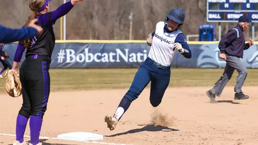 A softball player rounds third base towards homeplate against Holy Cross