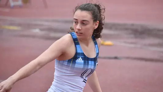 Izzie Anzaldo awaits the baton as she gets ready to run a relay in her white and blue track uniform.
