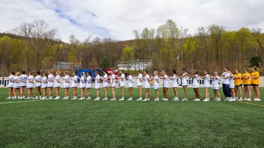 The women's lacrosse team lines up with their left arm on the next person's left shoulder during the national anthem.