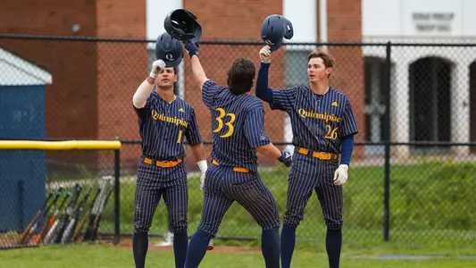 Three Quinnipiac baseball players tap their helmets together at home plate after a homerun