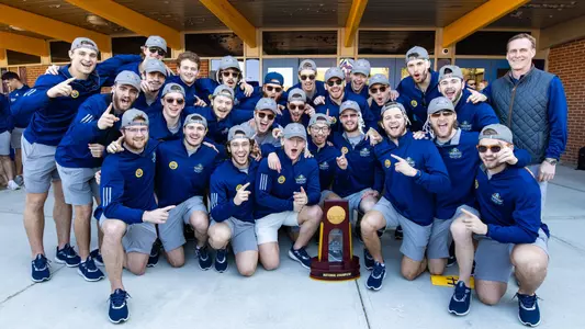 All men's ice hockey players, along with head coach Rand Pecknold, pose for a photo with the national championship trophy in front of M&T Bank Arena.