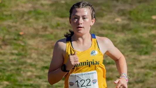 Rachel St. Germain looks forward and runs in her gold uniform with a navy Quinnipiac across the middle.