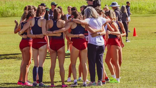 Women's Cross Country team huddled together with their backs to their camera, getting ready to race