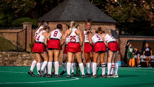 Field hockey team, wearing white jerseys and red skirts, huddle