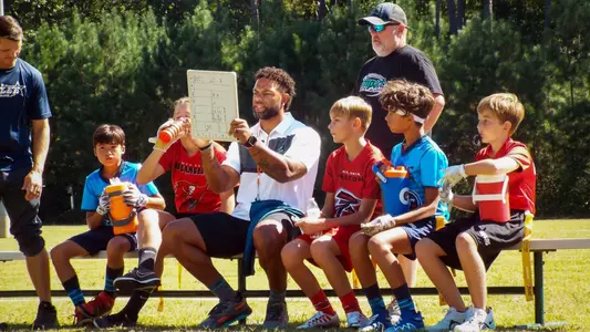 Stacy Tutt holds a whiteboard up in front of flag football players seated on a bench.