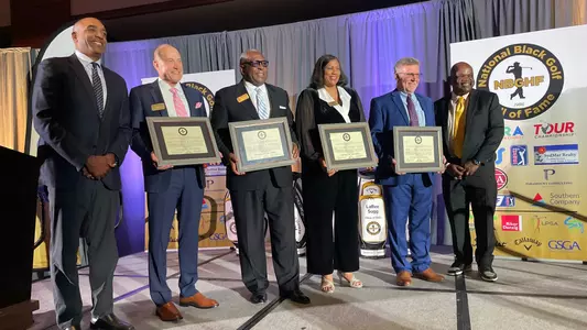 LaRee Sugg stands in the middle of stage holding a plaque recognizing her induction into the National Black Golf Hall of Fame.