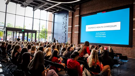 Wide angle of a large group of female student-athletes in Spider Hall for SPD's women's health symposium