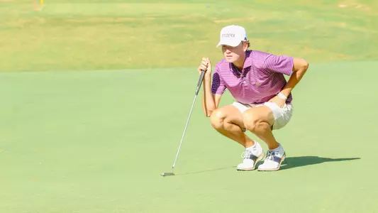 Drew Carlin squats to read a putt on the green.