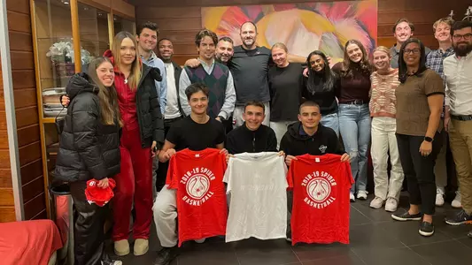 A group of UR student-athletes and staff pose with individuals in Greece