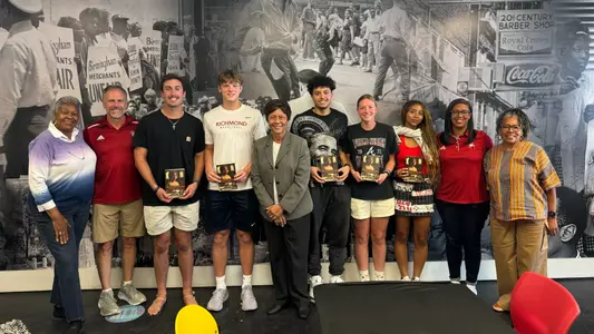 Students pose with athletic administrators in front of a mural