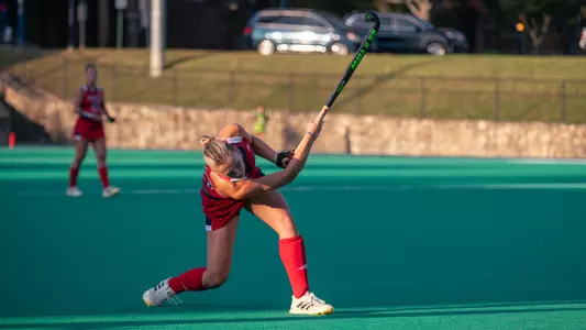 In an all-read Richmond uniform, Clara Larripa lifts the ball into the air down the field for Spider Hockey
