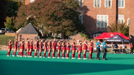 Spider Field Hockey in their all red uniforms, with goalkeepers in teal, stand for the National Anthem