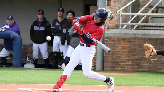 Jack Arcamone in a red number 12 jersey top and white pants swings at the baseball.