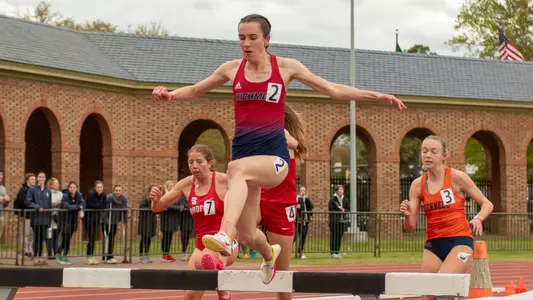 Elizabeth Stockman jumping over the bar in the steeplechase event, looking down at the water as she is getting ready to jump in it