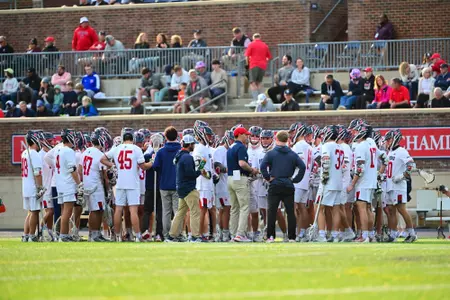 Men's lacrosse team on the sideline being talked to during a timeout by coaches