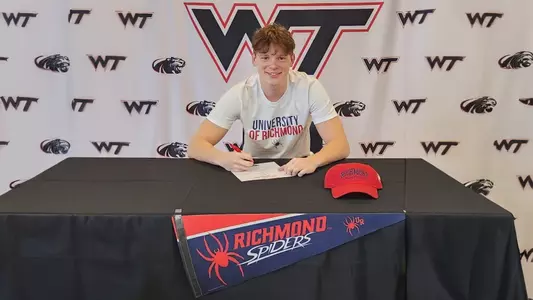 Kirby Mooney sits at a table and signs paperwork to attend the University of Richmond