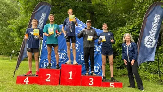 Podium at the 2024 National Trail Race, including Stuart Terrill at the first place marker, Jordan Bendura at 3rd, and Zach Stevens at 4th. Lori Taylor is standing next to the podium as well