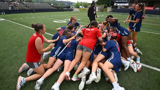 2024 Women's Lacrosse team jumping into a pile in the middle of the field after they won the Atlantic 10 Championship game