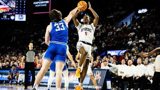 Collin Tanner shoots over a Saint Louis defender in front of the Saint Louis bench